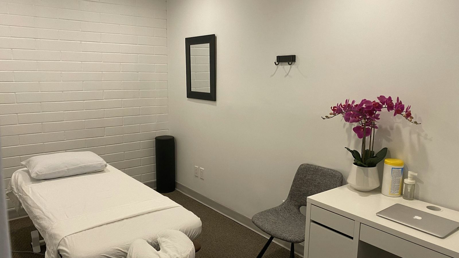 a treatment room with a made-up table, a chair and an orchid